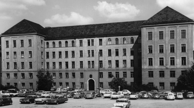 Jahr 1950; fünfstöckiges breites Bürogebäude mit großem Parkplatz davor, darauf stehen Autos aus den 50er Jahren